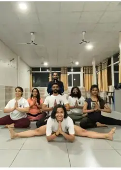 Students and a teacher sitting in prayer pose and a side split in the yoga hall